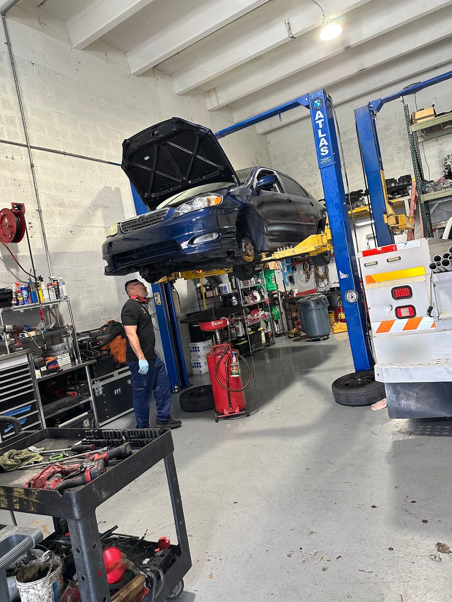A technician checks a blue Toyota Corolla raised on the lift inside RMJ's Bay A